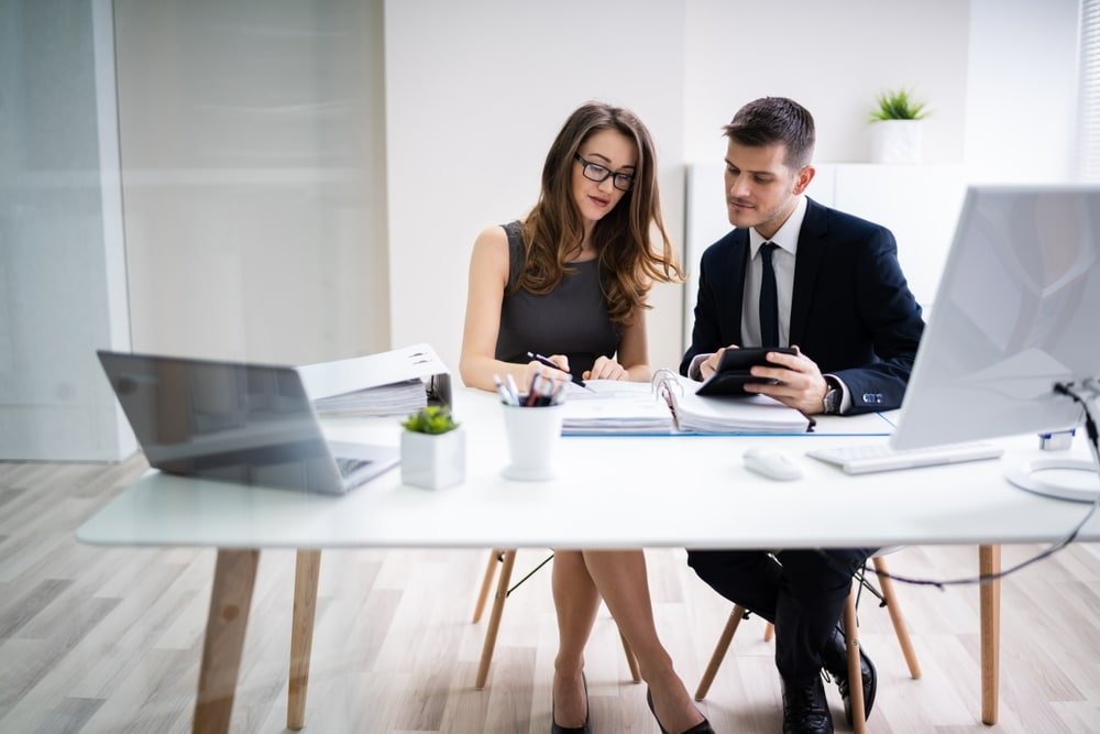 Two,Young,Businesspeople,Calculating,Invoice,With,Calculator